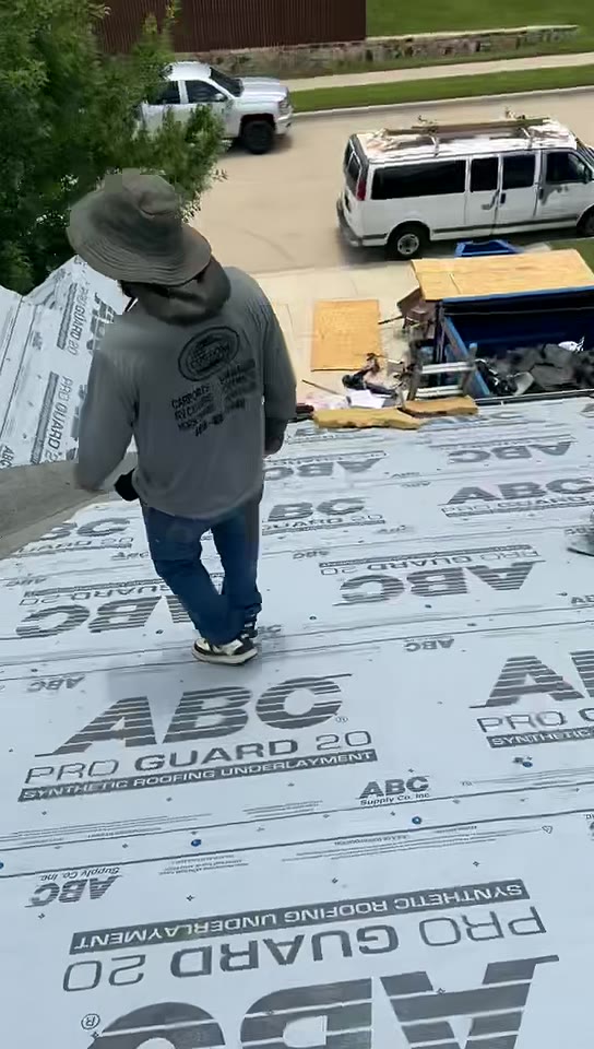 Roofer walking a roof deck covered in fresh synthetic underlayment with shingle bundles nearby